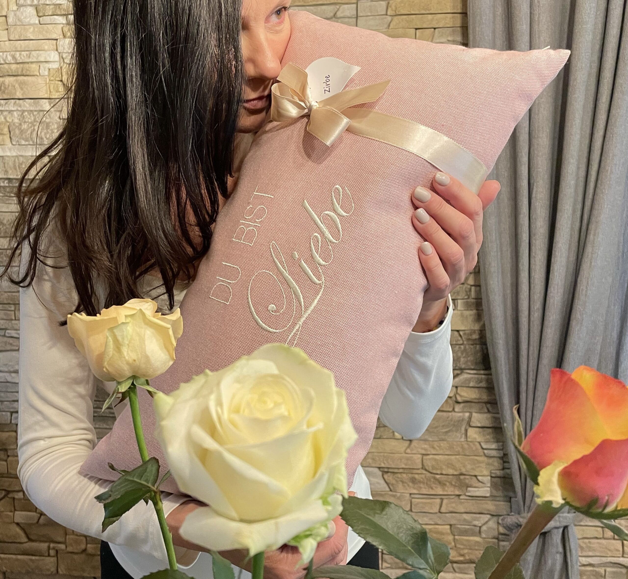 Du bist Liebe _ personalisierte Geschenke Personalisierte Geschenke in Form von Zirbenkissen. Frau hält ein personalisiertes Zirbesnkissen in der Hand und nimmt den Duft auf. Im Vordergrund die Rosen zum Geburtstag