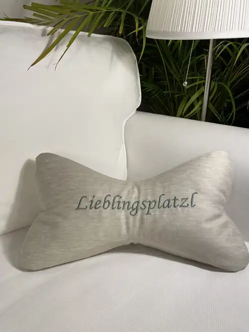 Leseknochen als Entspannungskissen mit waschbarem Halbleinenüberzug in Farbe natur. Personalisiert mit gestickten Buchstaben "LIEBLINGSPLATZERL" in hellblauer Farbe. Ansicht von vorne. In der Vertiefung kann der Kopf ganz angenehm abgelegt werden. Die Leseknochen sind geeignet um auf der Gartenliege zu entspannen und auch für den Thermenaufenthalt. Das Innenkissen ist mit getrockneten Lavendelblüten und Dinkelspelze gefüllt. Der Lavendelduft vertreibt Kopfschmerzen und die Dinkelspelze bringt den Knochen in Form und man kann den Kopf angenehm ablegen. Somit sind diese Kissen sehr gut als Nackenkissen geeignet um Verspannungen im Nackenbereich entgegenzuwirken.